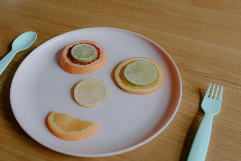 a white plate topped with slices of fruit next to a fork, by Emma Andijewska, trending on unsplash, process art, cute faces, silicone cover, orange pastel colors, on a wooden plate