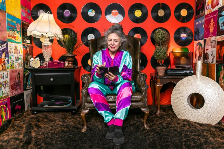 a woman sitting in a chair in front of a record wall, maximalism, wearing pajamas, betty white, andrew dickson, full device