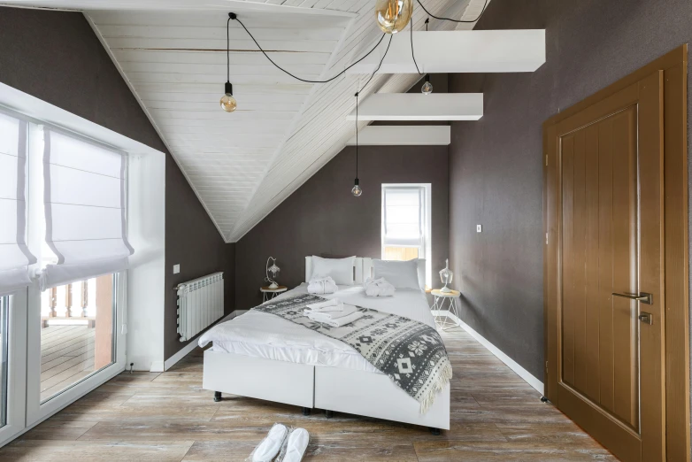 a white bed sitting in a bedroom next to a window, inspired by Willem Claeszoon Heda, trending on unsplash, light and space, peaked wooden roofs, charcoal and silver color scheme, light - brown wall, wide-angle view