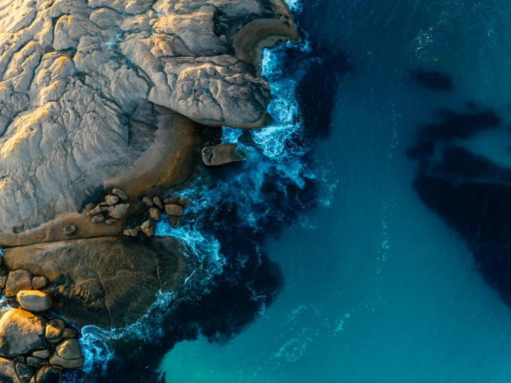 an aerial view of a body of water surrounded by rocks, by Jesper Knudsen, pexels contest winner, black cyan gold and aqua colors, a photo of the ocean, warm shades of blue, helicopter view