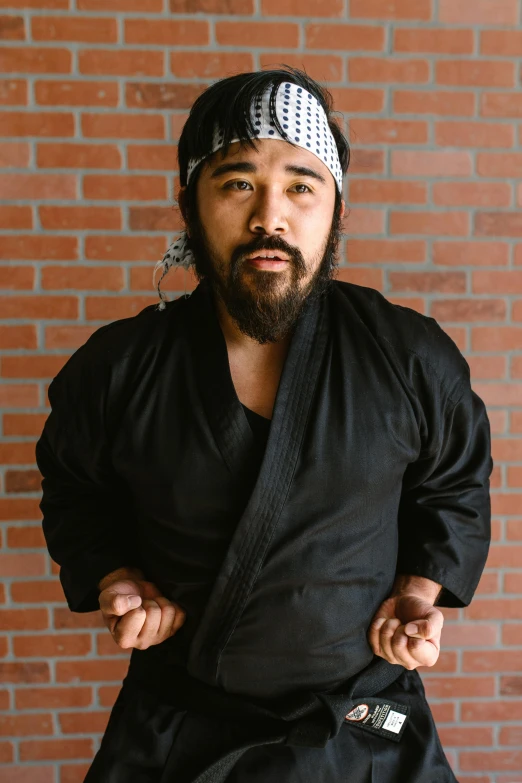 a man standing in front of a brick wall, a portrait, inspired by Kanō Sanraku, reddit, in a dojo, photo from a promo shoot, square, high quality photo