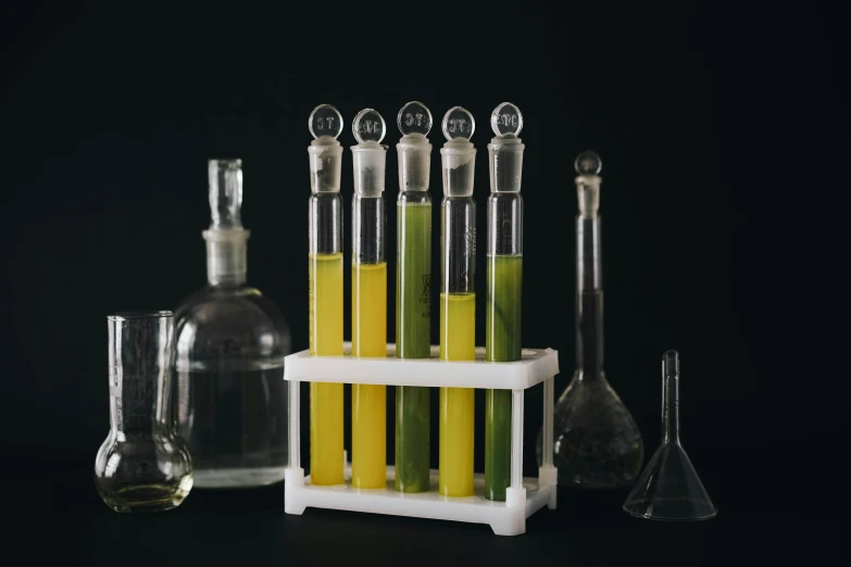 a bunch of test tubes sitting on top of a table, inspired by Ceferí Olivé, cooking oil, on black background, algae, yellow