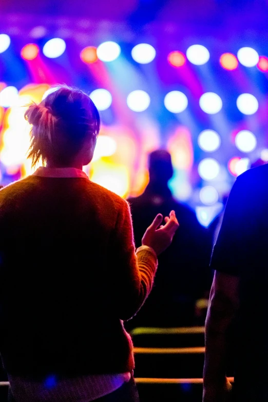 a group of people standing in front of a stage, by Matt Cavotta, pexels, happening, neon glow soft bokeh, listening to godly music, a colorful, bokeh. brian spilner