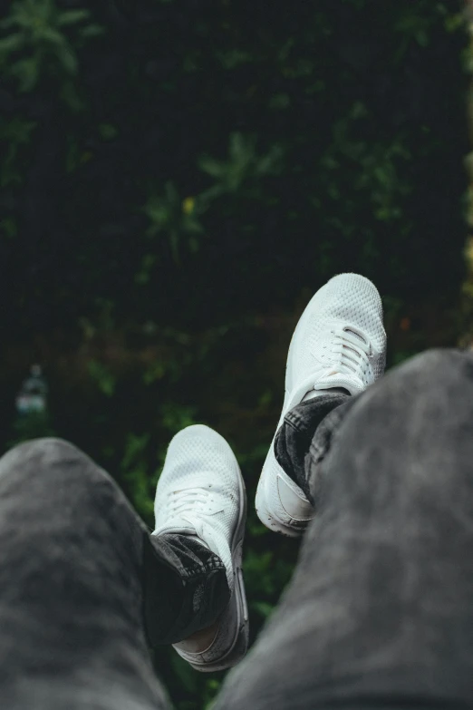 a person standing on a ledge with their feet in the air, trending on pexels, white and grey, sitting in the garden, looking down at you, sneaker photo