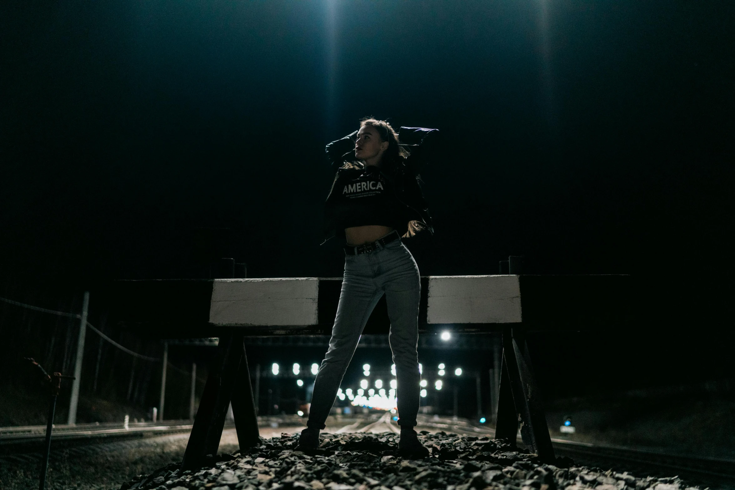 a woman standing on top of a train track at night, an album cover, pexels contest winner, pokimane, wearing jeans and a black hoodie, wearing a crop top, shooting pose