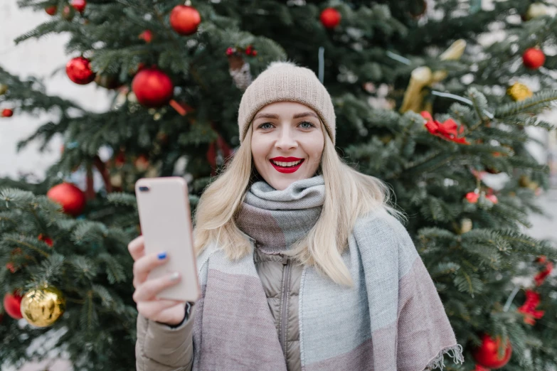 a woman taking a selfie in front of a christmas tree, trending on pexels, beautiful nordic woman, avatar image, outdoor photo