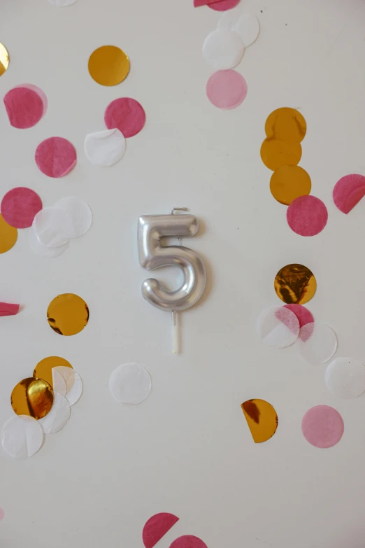 a white plate topped with a number five surrounded by confetti, by Nicolette Macnamara, trending on unsplash, satin silver, ffffound, birthday cake, inflateble shapes