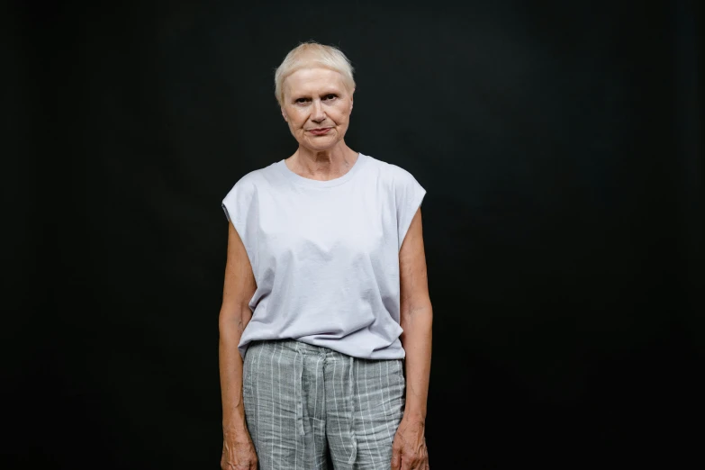 a woman standing in front of a black background, a character portrait, unsplash, elderly, wearing pants and a t-shirt, may gibbs, 15081959 21121991 01012000 4k