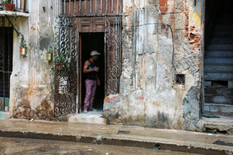 a man standing in a doorway of an old building, by Gina Pellón, 30-year-old woman from cuba, wet streets, thumbnail, a wide full shot