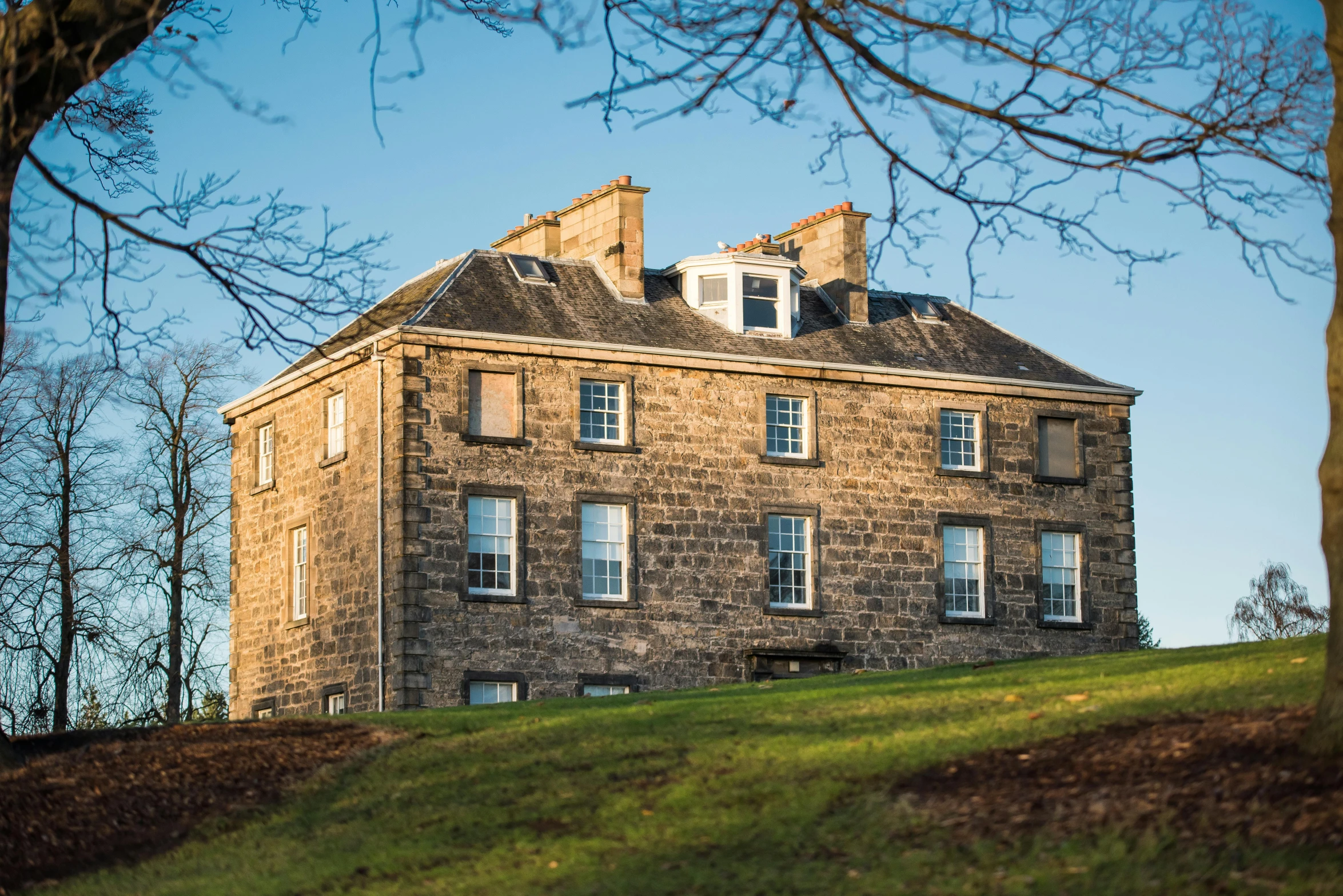 a large stone building sitting on top of a lush green hillside, by Gawen Hamilton, renaissance, winter sun, exterior view, family friendly, front elevation view