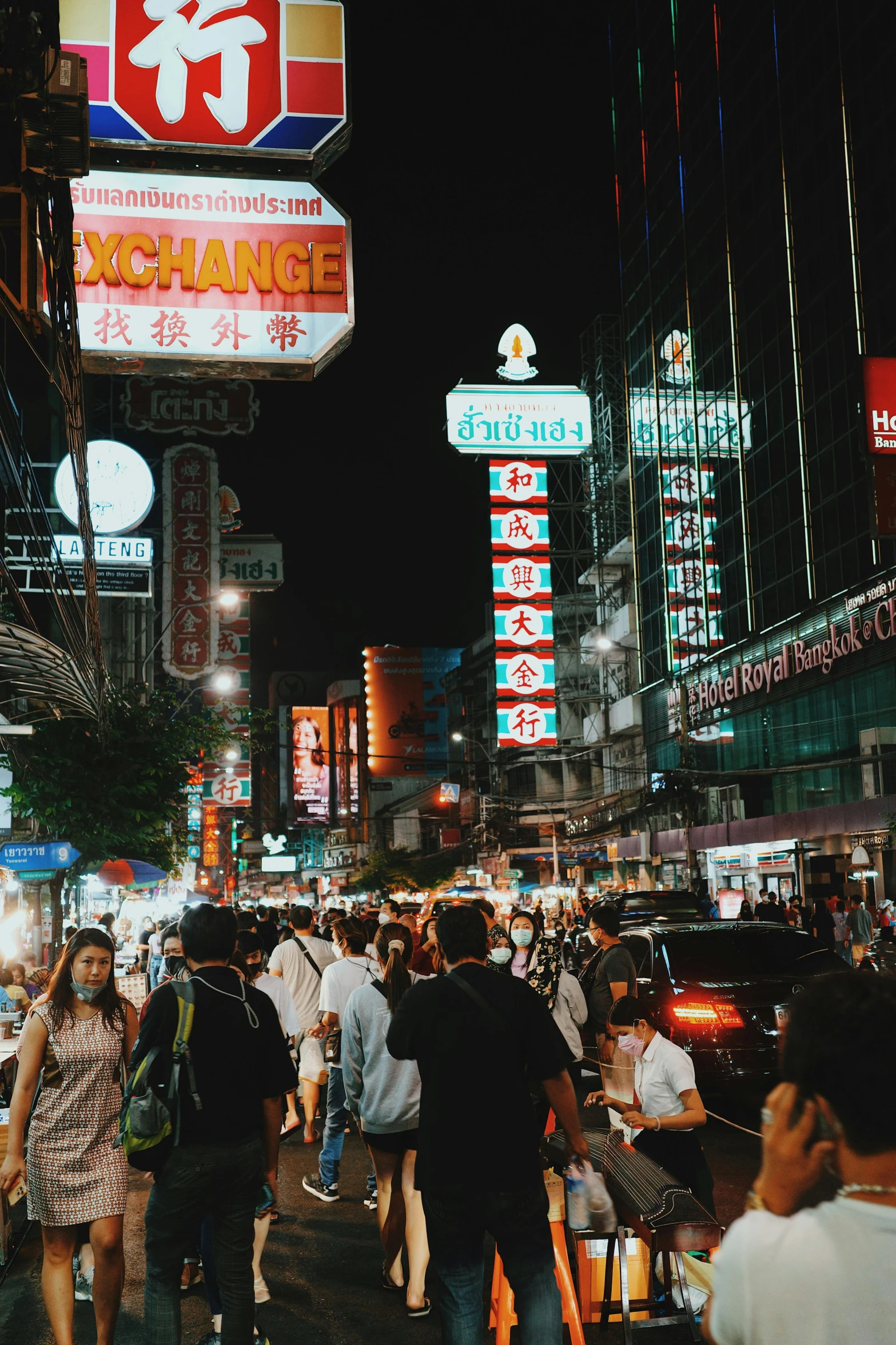 a group of people walking down a street at night, bangkok, street signs, neon signs in the distance, city