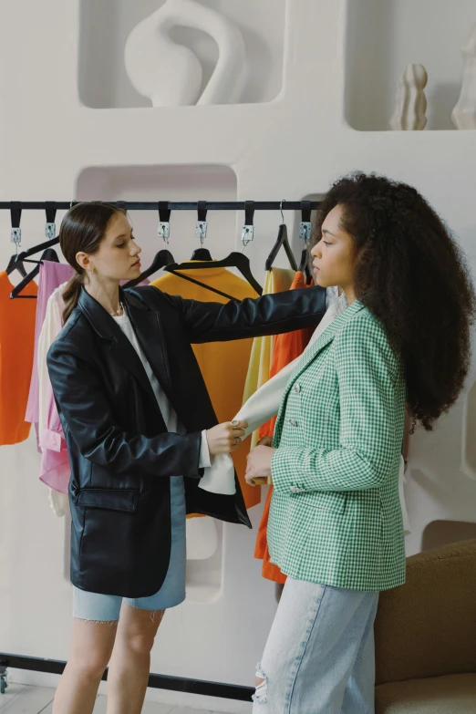 two women standing in front of a rack of clothes, trending on pexels, renaissance, giving an interview, wearing a fancy jacket, promo image, people at work