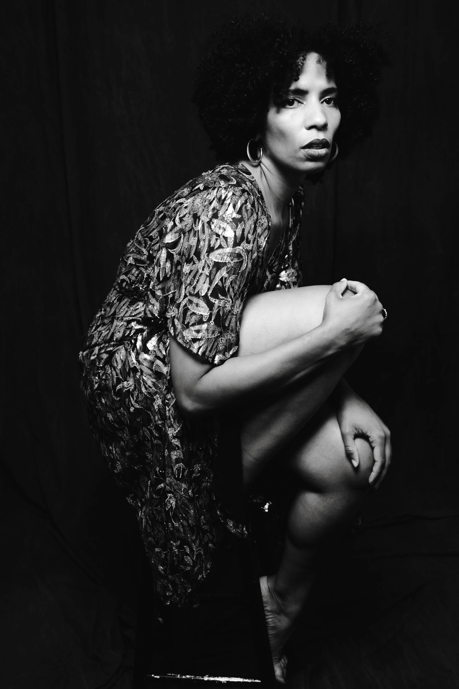 a black and white photo of a woman squatting on a stool, realism, afropunk, in a dress, studio photoshoot, androgynous