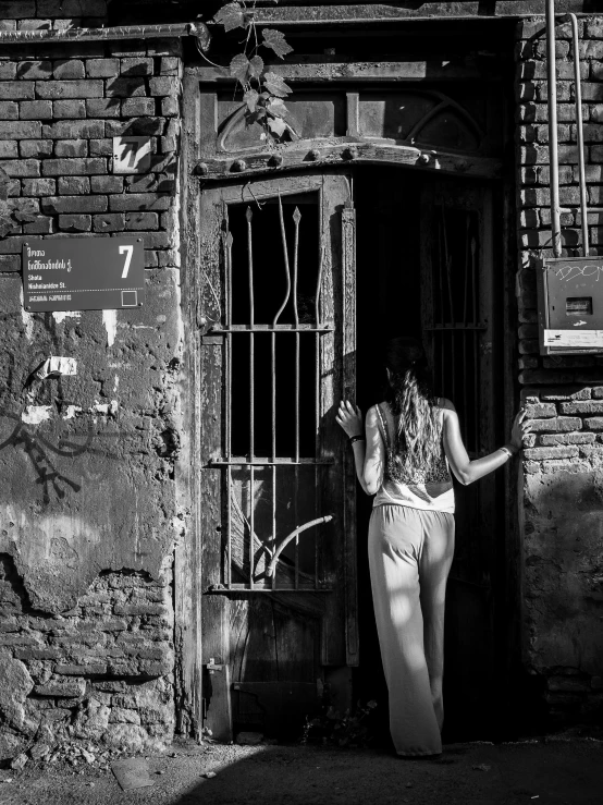 a woman standing in the doorway of a building, by Michalis Oikonomou, fallout style istanbul, ((((dirt brick road)))), the woman is behind bars, alexey gurylev