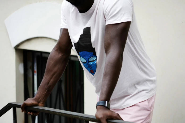 a man in a white shirt leaning on a railing, by Jessie Alexandra Dick, pexels contest winner, afrofuturism, batman t shirt, man with a blue heart, black face, slightly pixelated