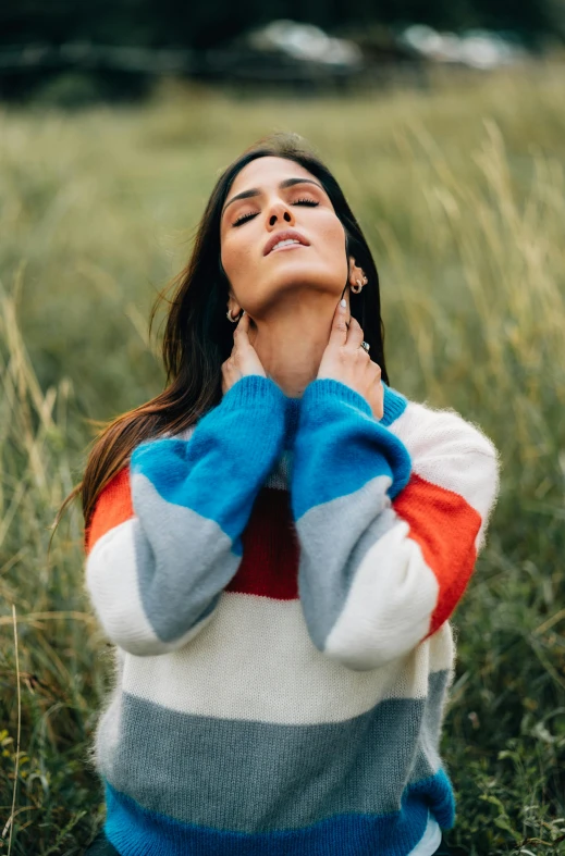 a woman sitting in a field of tall grass, a portrait, by Robbie Trevino, trending on pexels, color field, striped sweater, blue and orange, dua lipa, peruvian looking