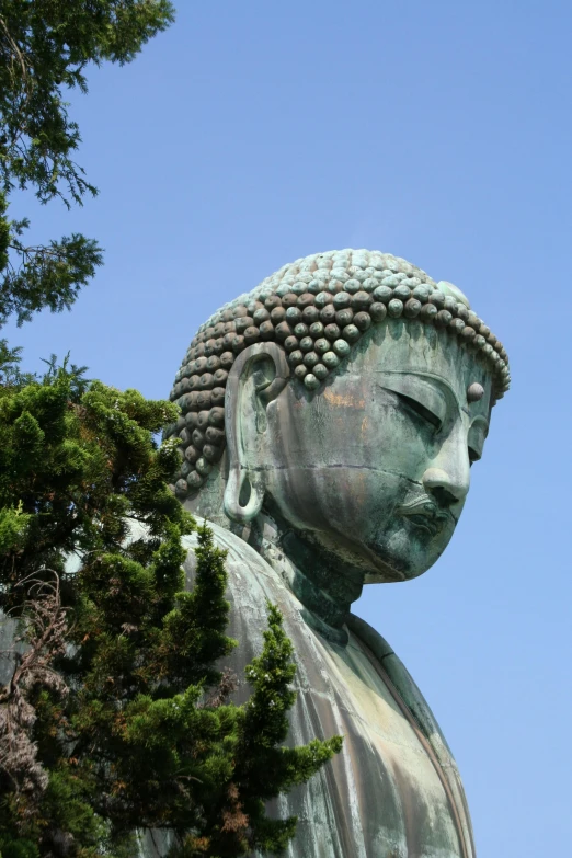 a close up of a statue with trees in the background, a statue, sōsaku hanga, buddhist architecture, blue sky, looking serious, round portruding chin