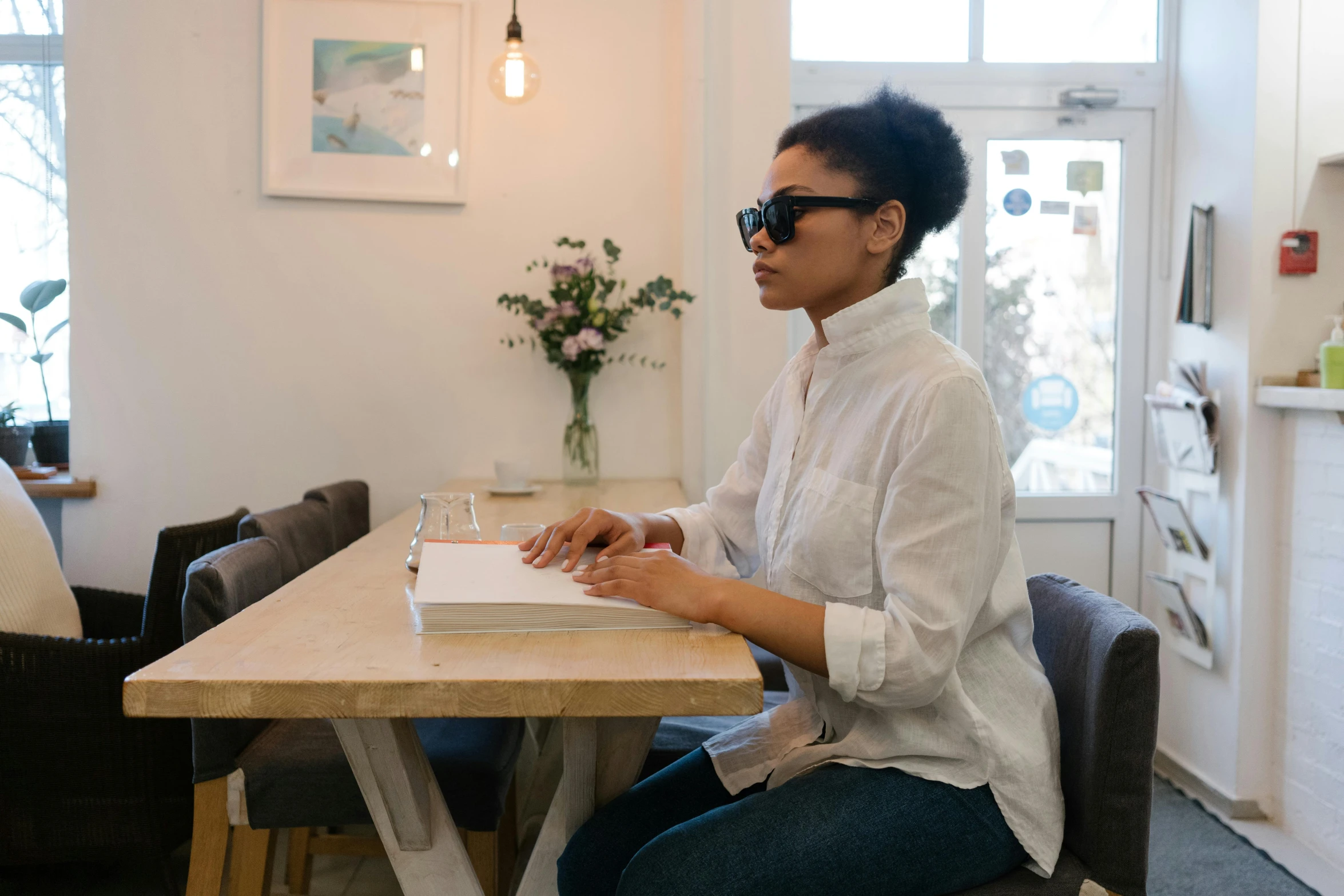 a woman sitting at a table with a book, trending on unsplash, private press, implanted sunglasses, a very macular woman in white, ashteroth, papers on table