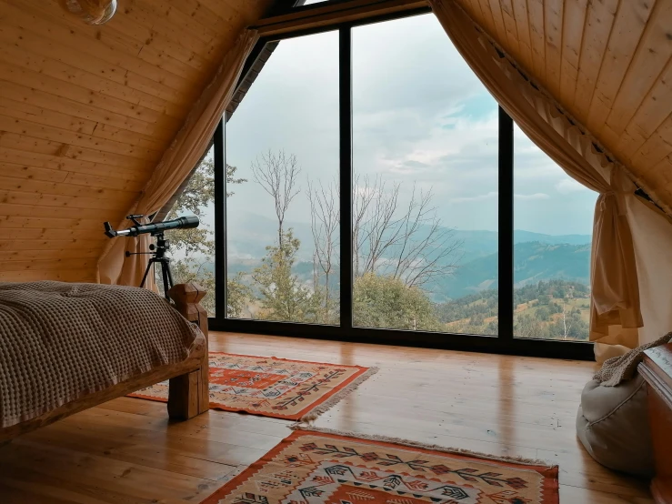 a bed sitting inside of a bedroom next to a window, by Muggur, pexels contest winner, log houses built on hills, persian rugs, panoramic view, inside a cozy apartment