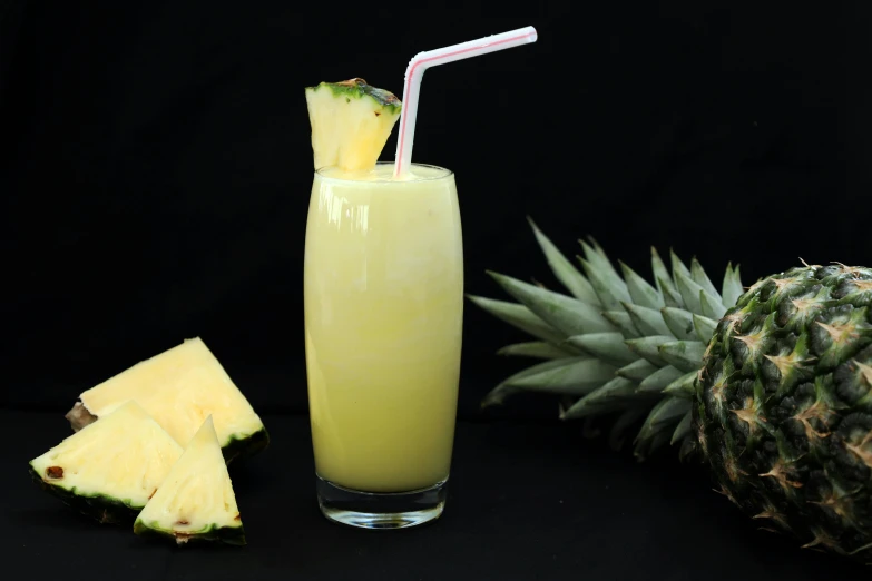 a glass of pineapple juice next to a pineapple, pexels, various posed, in front of a black background, yellow mist, straw