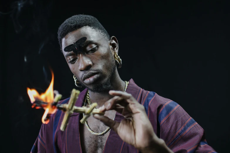 a man lighting a match with a matchstick, an album cover, inspired by Godfrey Blow, trending on pexels, afrofuturism, playboi carti portrait, mkbhd, wears a egyptian ankh necklace, shot in the photo studio