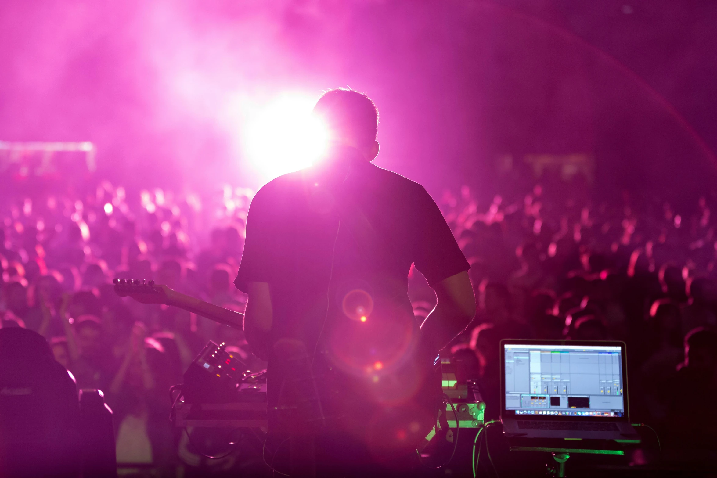 a man that is standing in front of a laptop, pexels, happening, at a rave, haze over the shoulder shot, playing guitar onstage, back - lit