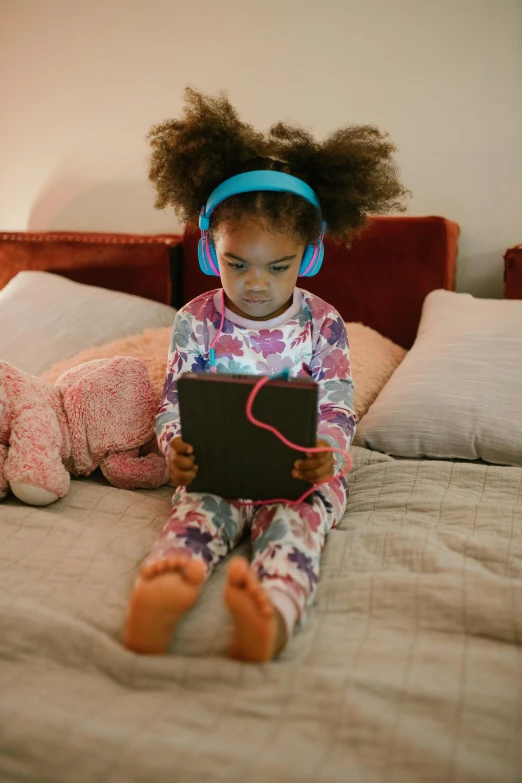 a little girl sitting on a bed with headphones on, slate, thumbnail, afro tech, using a magical tablet