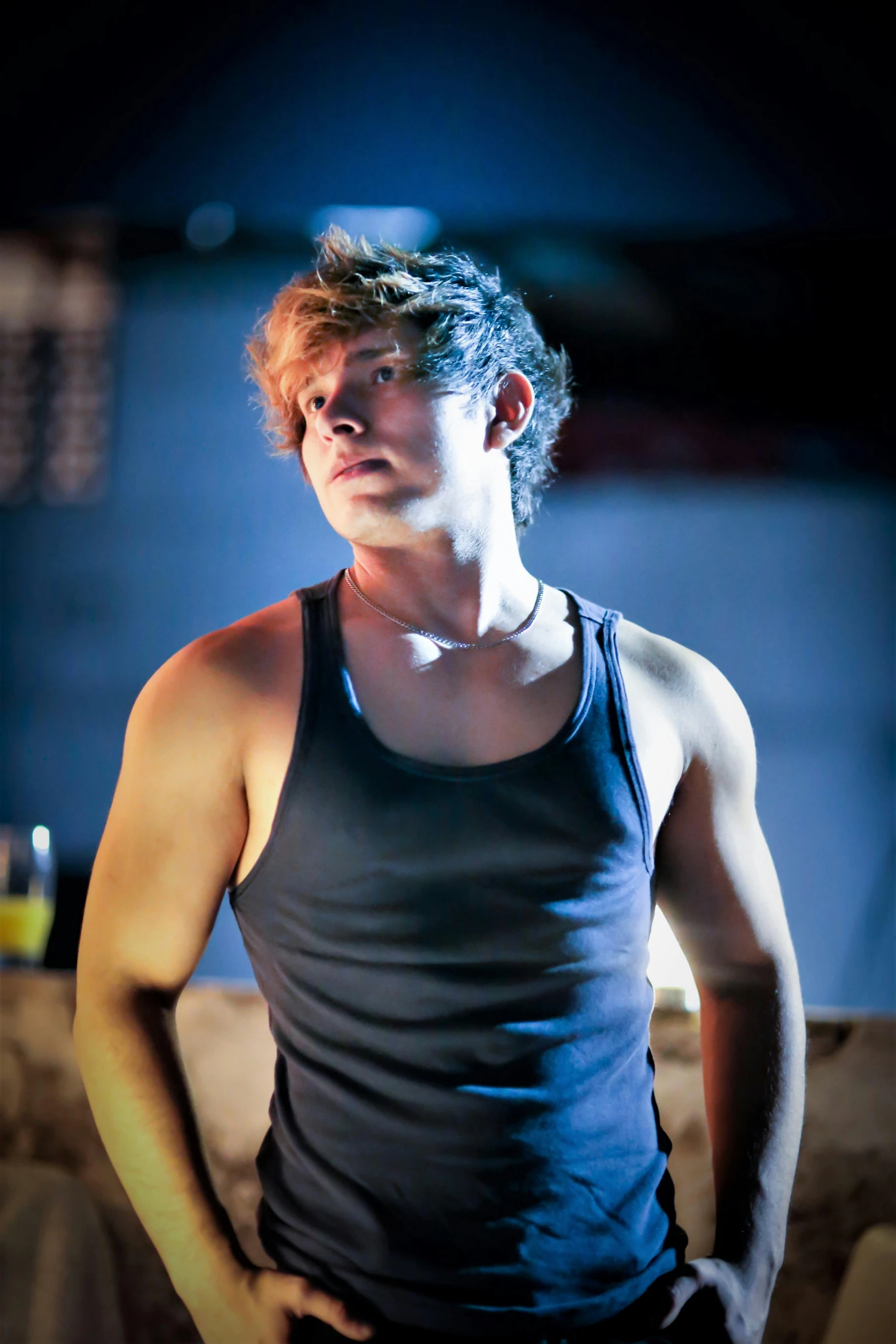 a man in a tank top sitting on a couch, inspired by John Luke, dramatic intense lighting, performing on stage, profile image, cool tousled hair