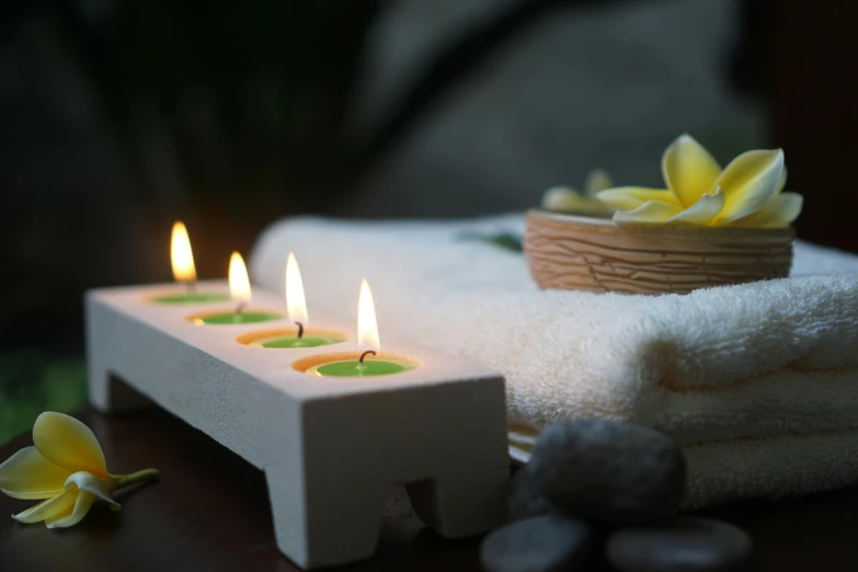 a pile of white towels sitting on top of a table, holding a candle holder, paradise garden massage, colour photograph, wooden