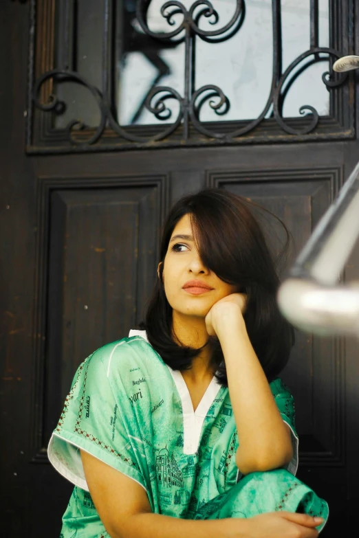 a woman sitting in front of a door next to a lamp, an album cover, by Basuki Abdullah, unsplash, hurufiyya, freida pinto, sea - green and white clothes, bae suzy, candid portrait photo