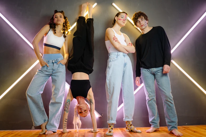 a group of people standing on top of a wooden floor, trending on pexels, antipodeans, baggy jeans, with neon lighting, avatar image, acrobatic pose