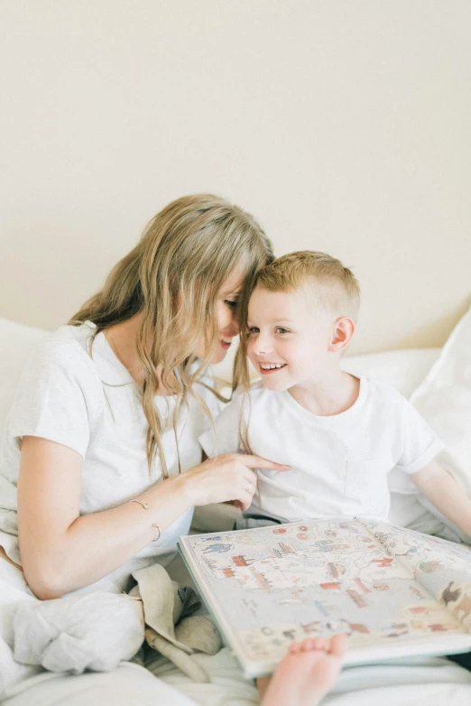 a woman reading a book to a child on a bed, a picture, pexels contest winner, board game, wearing white pajamas, profile image, blonde