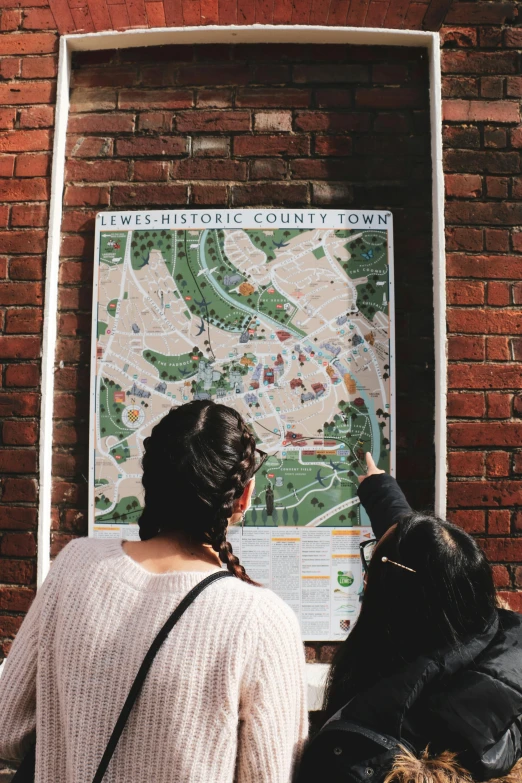 two women looking at a map on a brick wall, a poster, by David Brewster, pexels, interactive art, barnet, high view, square, sign
