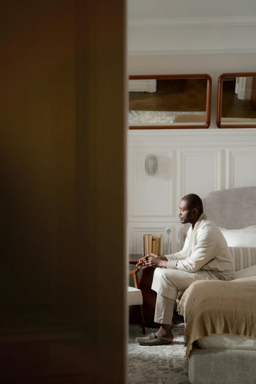 a man sitting on a bed in a room, inspired by Barthélemy Menn, wearing white pajamas, lebron james, architectural digest, hammershøi