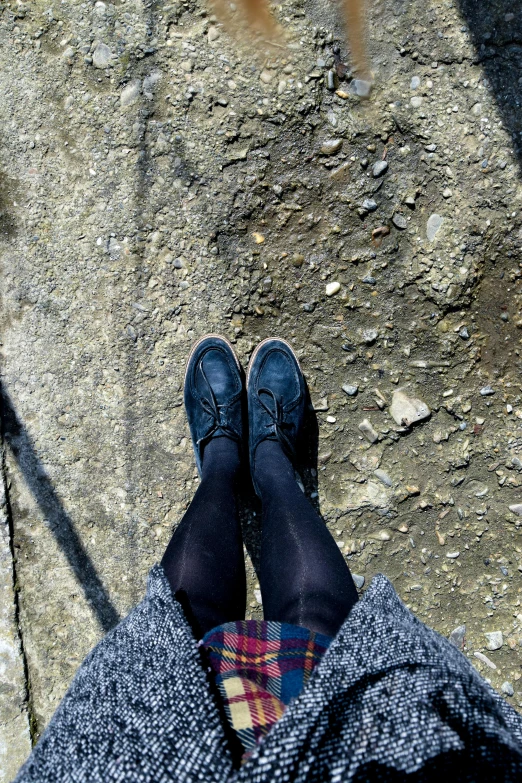 a person standing on a sidewalk with their feet up, a picture, blue and black, creepers, stand on stone floor, wearing dirty travelling clothes