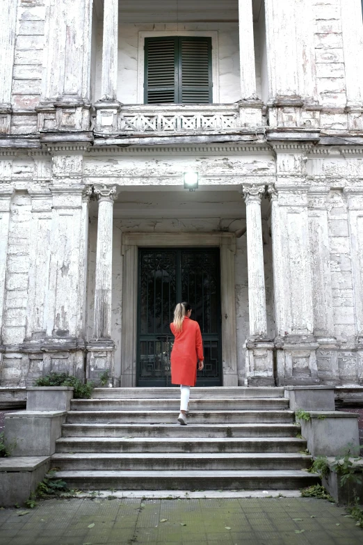 a woman in a red coat standing in front of a building, a statue, inspired by Piero della Francesca, bengal school of art, 2019 trending photo, doorway, white and orange, nepali architecture buildings