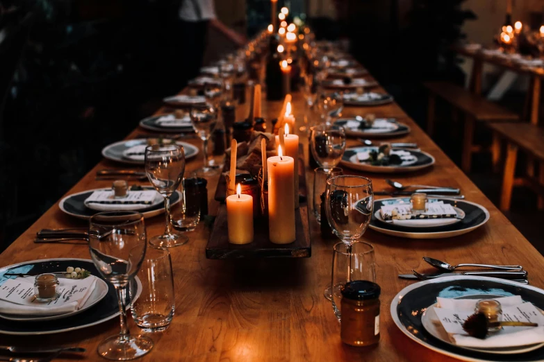 a long wooden table topped with plates and candles, by Carey Morris, pexels contest winner, sydney hanson, waxy candles, casually dressed, fiona staples