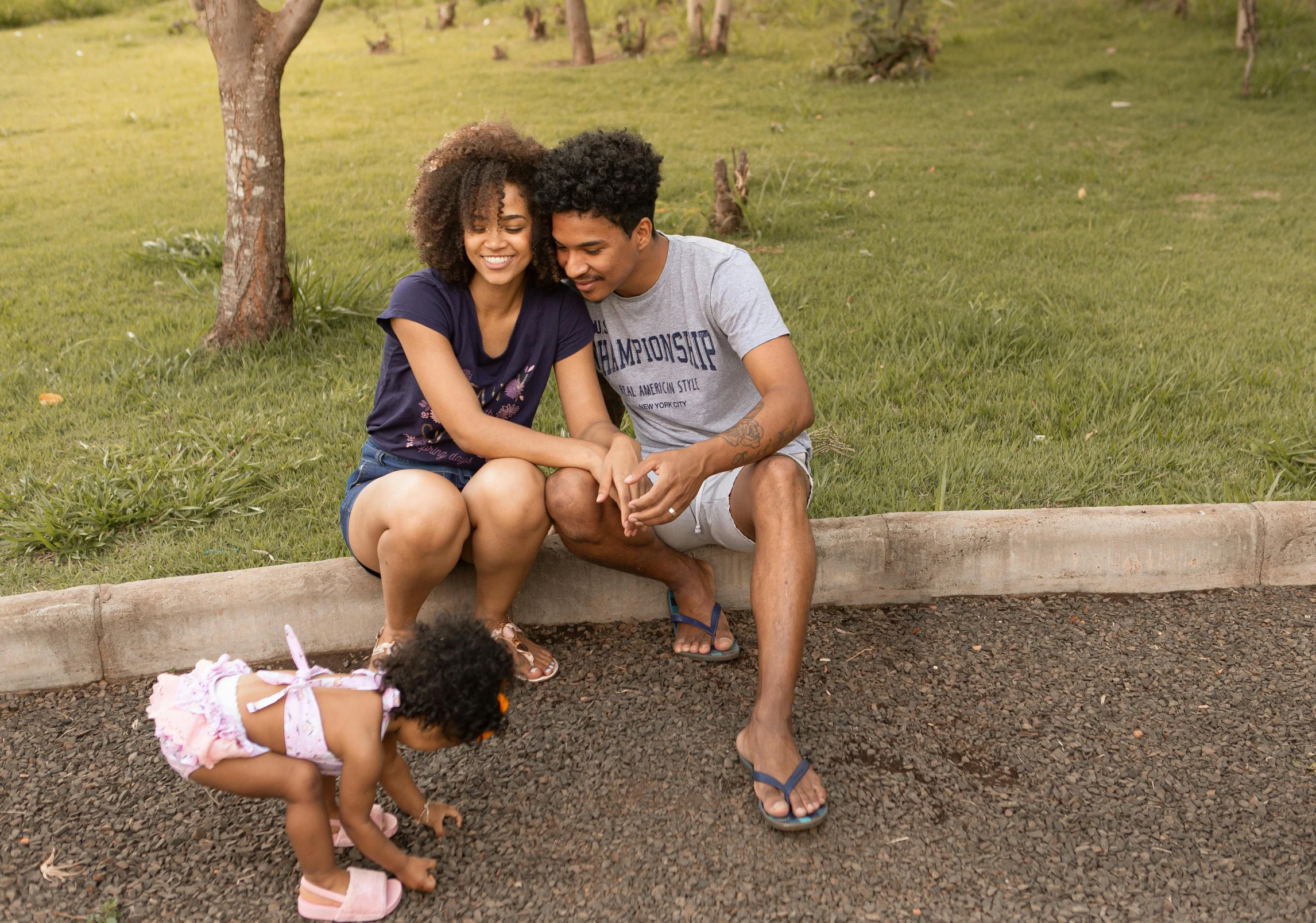 a man and woman sitting next to a small child, pexels, happening, tan skin a tee shirt and shorts, parks, with afro, gravels around