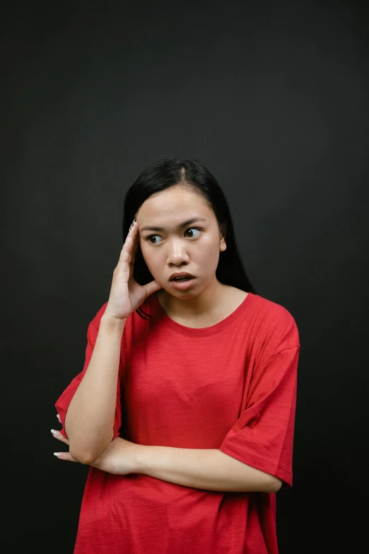 a woman in a red shirt posing for a picture, trending on pexels, confused facial expression, asian human, black backdrop, distraught