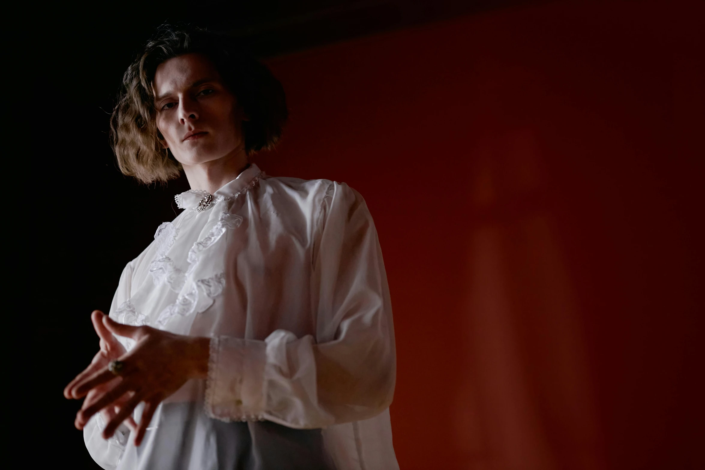 a woman standing in front of a red wall, inspired by Jan Lievens, unsplash, bauhaus, with victorian clothing, film still from horror movie, androgynous male, wearing white silk