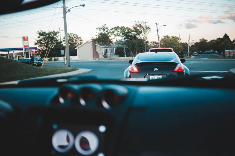 a car driving down a street next to a gas station, unsplash, sportscar, view from behind, inside of a car, casually dressed
