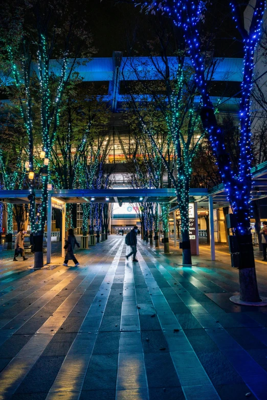 a street filled with lots of trees covered in blue lights, inspired by Miyagawa Chōshun, happening, at a mall, cozy environment, sakimichan hdri, lamps on ground