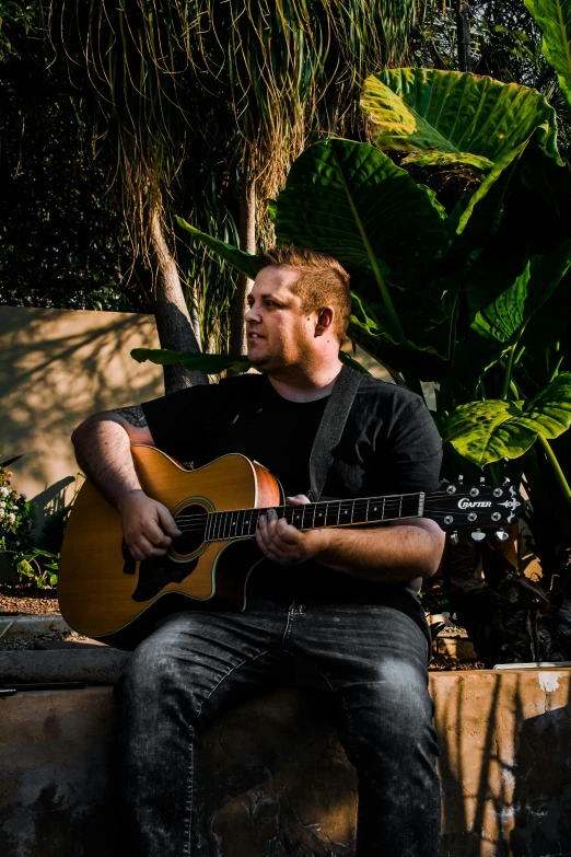 a man that is sitting down with a guitar, lachlan bailey, in the garden, with backdrop of natural light, scott wozniak