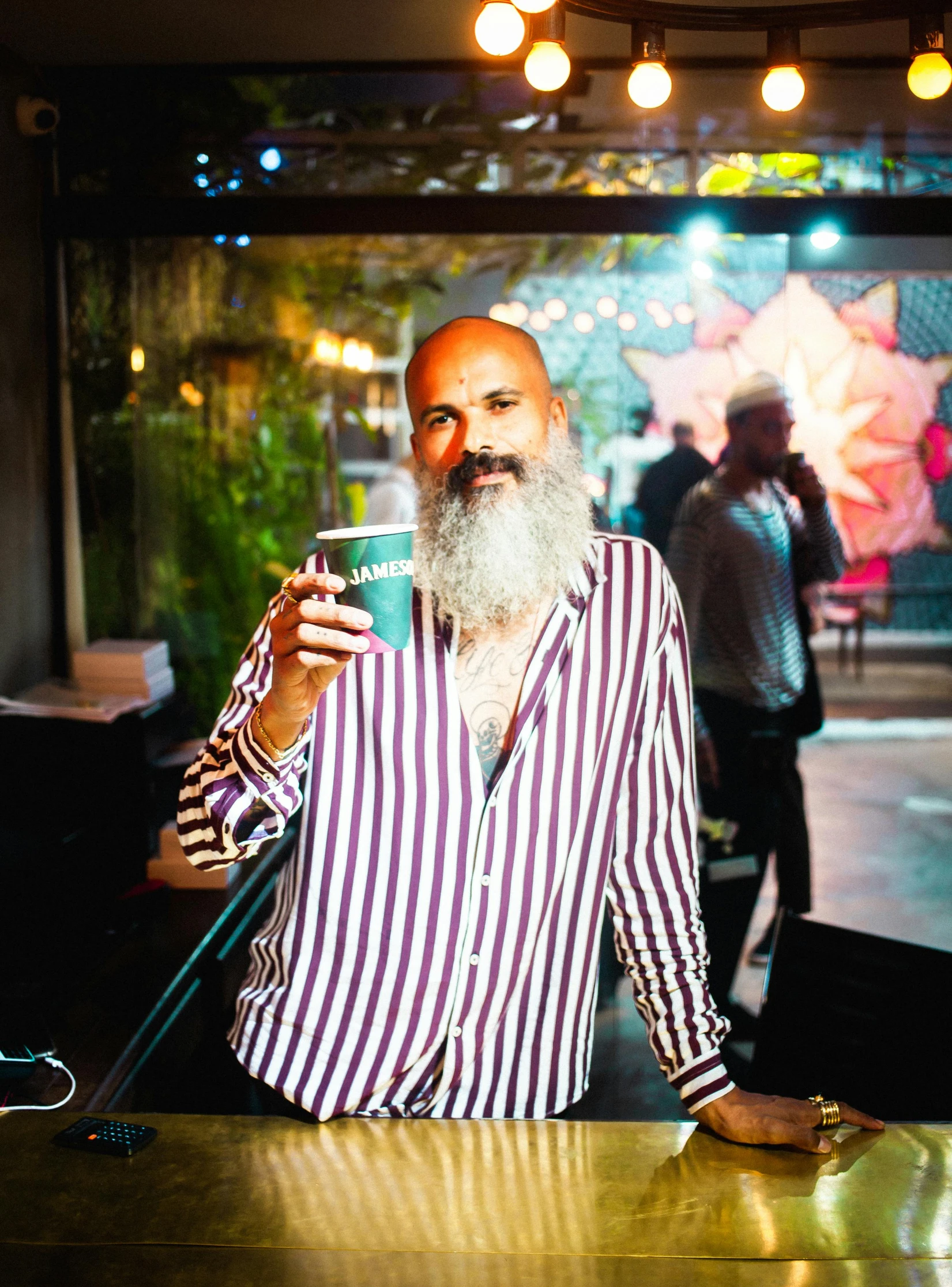 a man sitting at a bar using a cell phone, an album cover, unsplash, happening, full white beard, temuera morrison, holding a drink, standing still