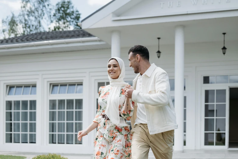 a man and a woman walking in front of a house, a colorized photo, pexels contest winner, hurufiyya, white hijab, background image, excitement, still image from the movie