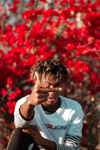 a man sitting in front of a bunch of red flowers, an album cover, pexels contest winner, hand gesture, black teenage boy, young thug, red trees