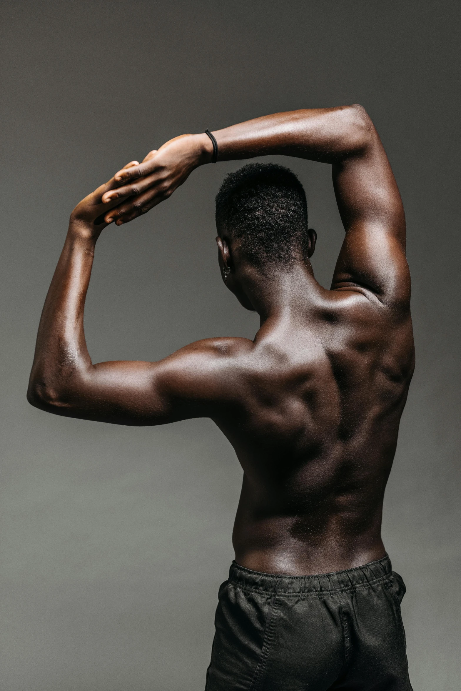 a man standing in front of a gray background, by Jessie Alexandra Dick, pexels contest winner, renaissance, showing her shoulder from back, man is with black skin, male calisthenics, indistinct man with his hand up