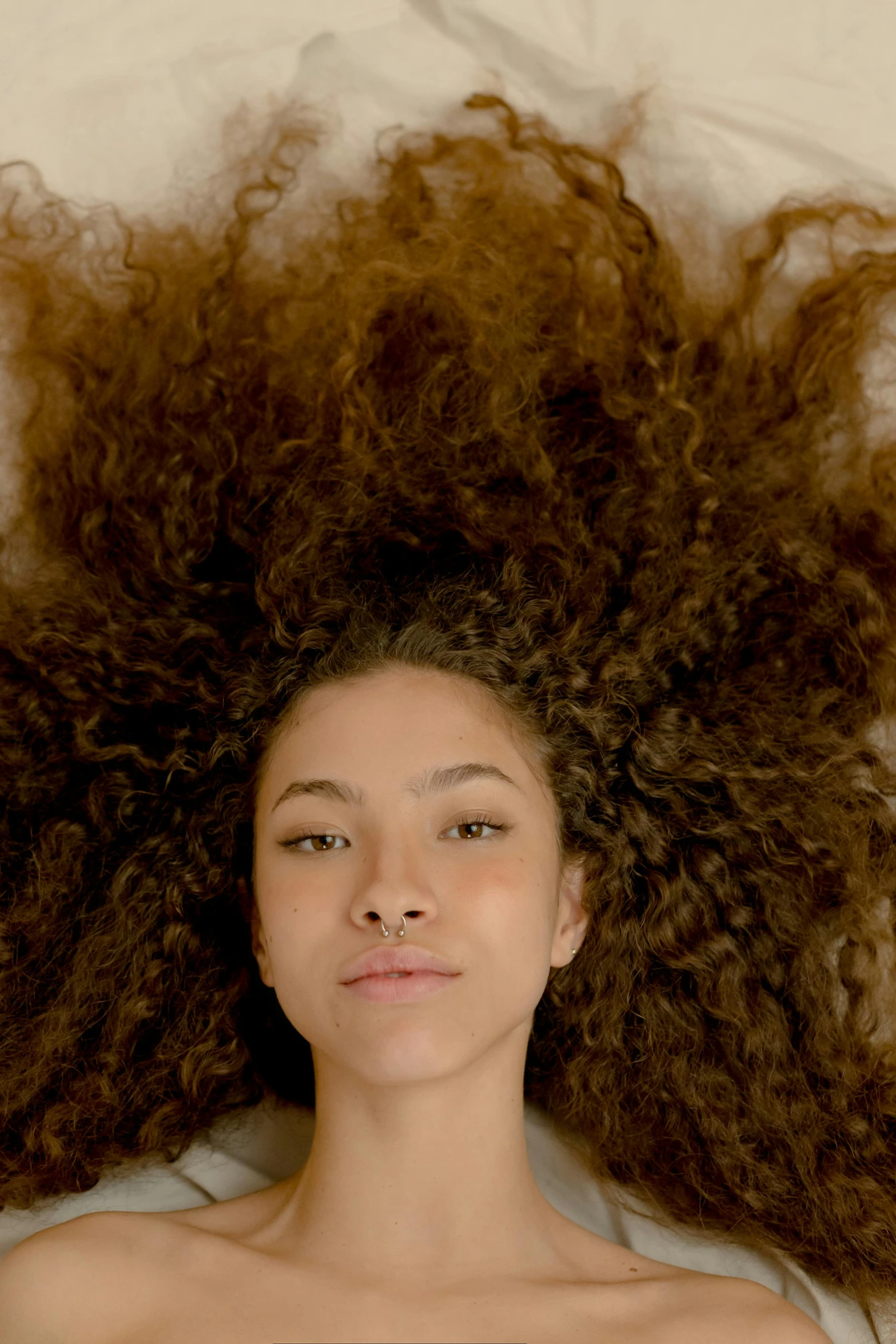 a beautiful young woman laying on top of a bed, trending on pexels, renaissance, flowing massive hair, mixed race, zoomed in, ignant