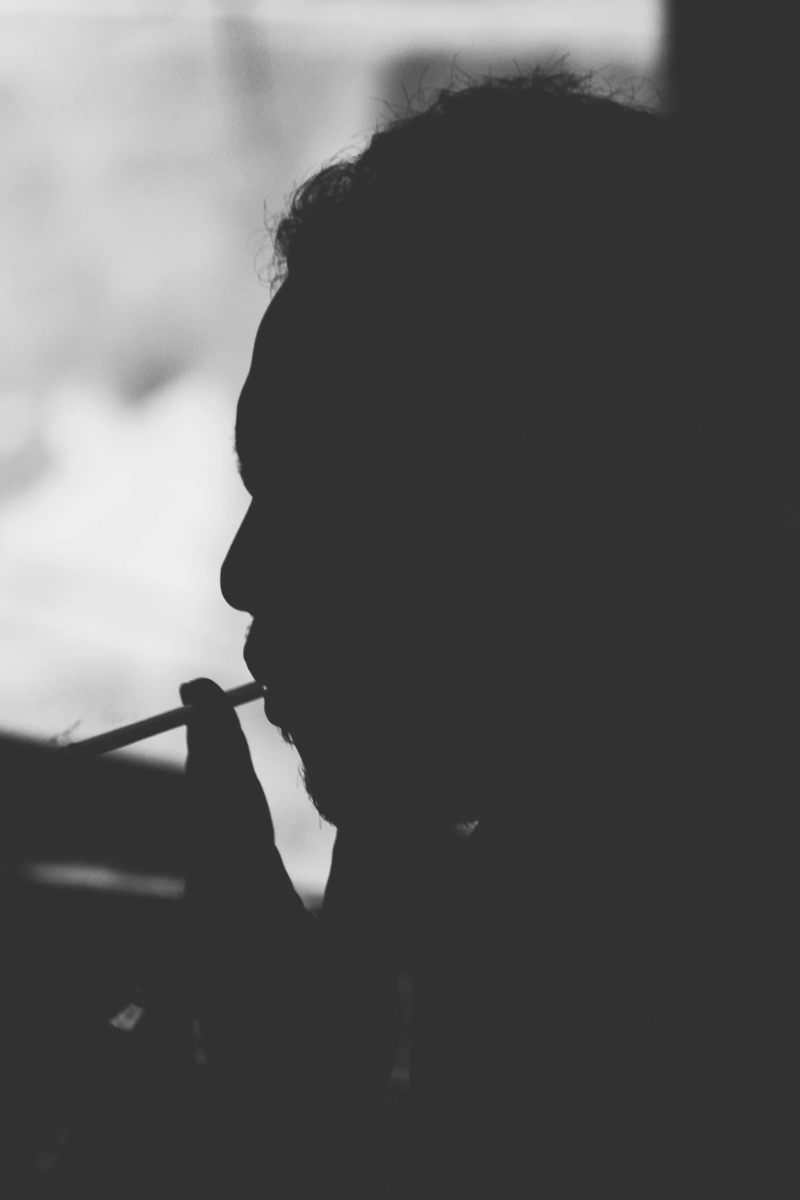 a person smoking a cigarette in front of a window, a black and white photo, by Adam Marczyński, unsplash, silhouette :7, donald glover, people's silhouettes close up, multiple stories