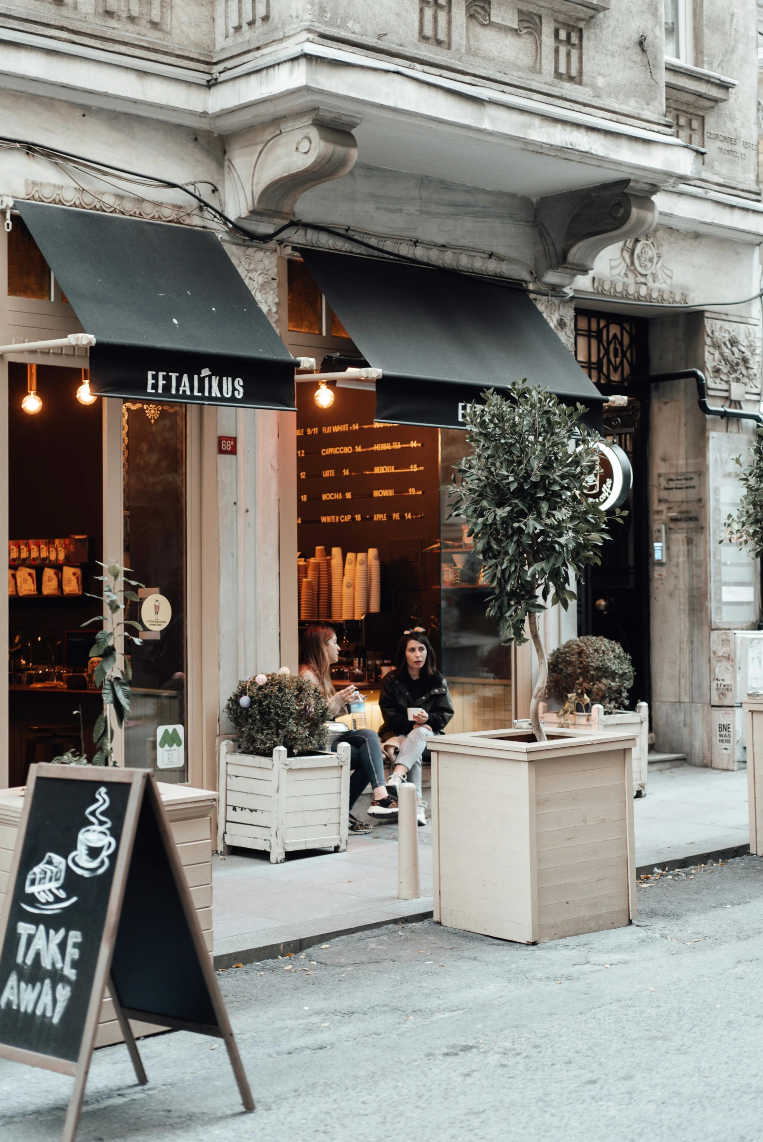 a person sitting on a bench in front of a store, expensive restaurant, lerapi, curated collections, side fed